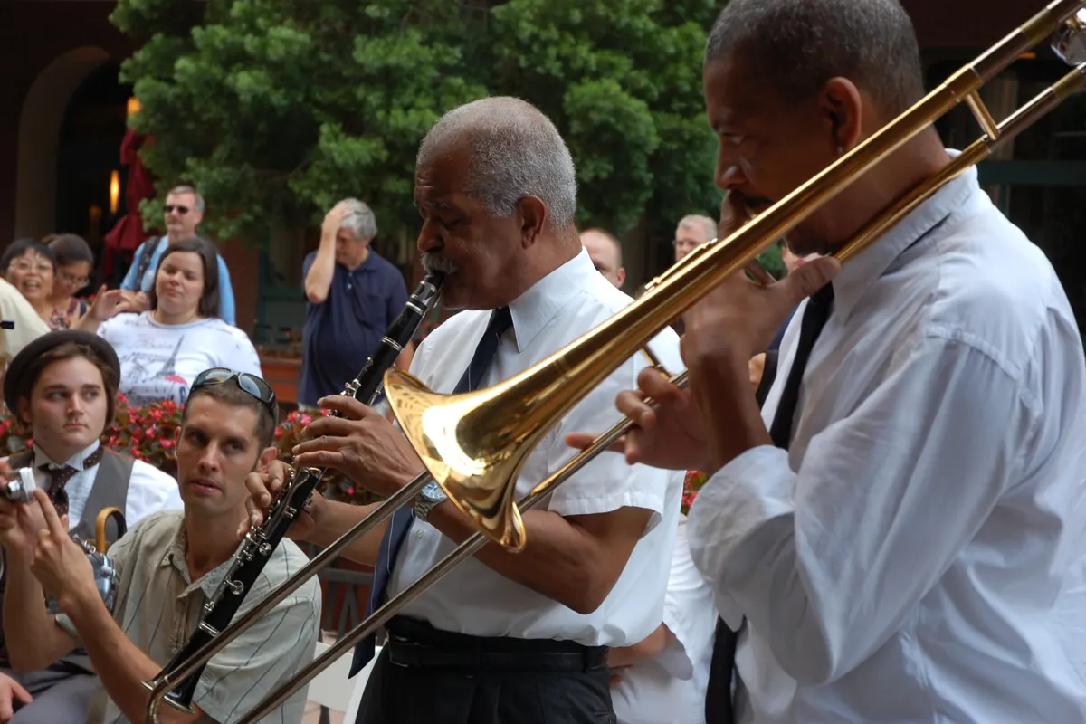 Un clarinettista e un trombonista in camicia bianca e cravatta che suonano all'aperto per un pubblico seduto a un concerto di jazz tradizionale di New Orleans