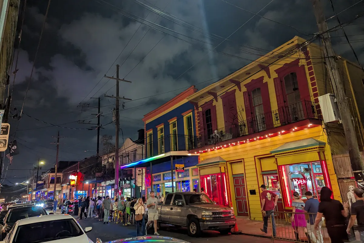 Frenchmen Street di notte, con edifici vivacemente dipinti di rosso, blu e giallo, insegne al neon e una fila di persone sul marciapiede sotto un cielo scuro e nuvoloso