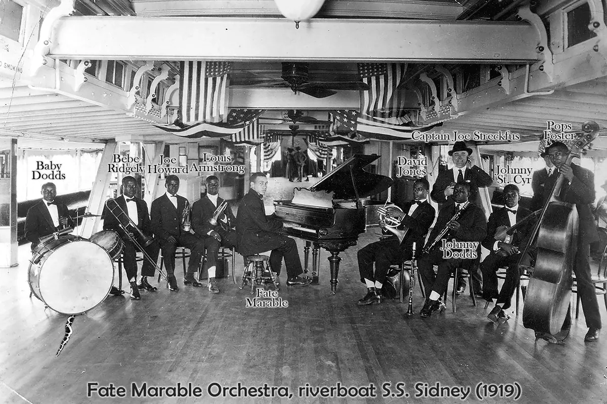 Fotografia in bianco e nero della Fate Marable Orchestra sul piroscafo Sidney nel 1919: musicisti in abito con batteria, un pianoforte a coda, fiati e un contrabbasso sotto bandiere appese